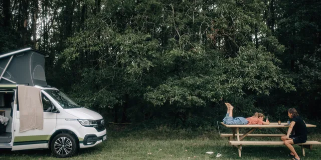 Vater und Tochter chillen an Holztisch beim Camping in Natur