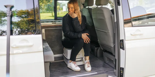 Eine Frau sitzt voll angezogen im Innern eines Campers auf einer Campingtoilette. In diesem Artikel erfährst du das Wichtigste zum Thema Chemietoilette entsorgen.