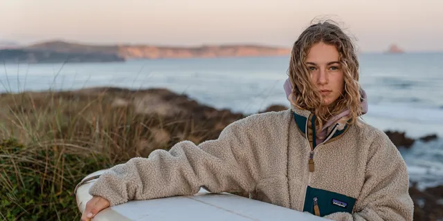 A girl with a surfboard surrounded by sand dunes.