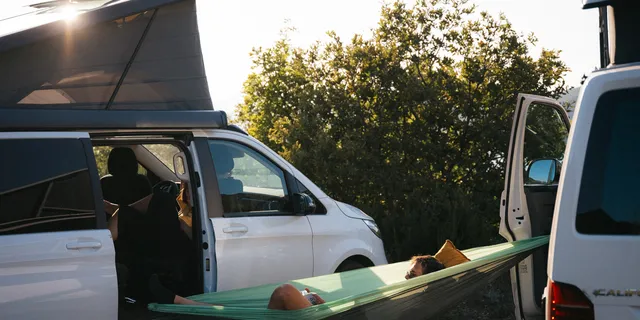 A man is lying in a hammock between campers.