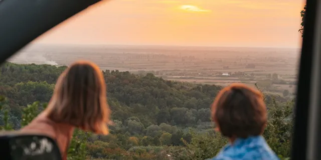 Two friends are sitting in front of their camper, watching the sunset over Albania during their Albania road trip.