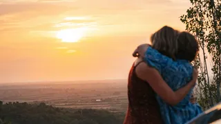 Gay Travel Index: A lesbian couple hugging alongside their camper during sunset.