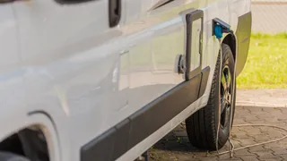 The power connection of a white motorhome from which a charging cable on the ground leads to the CEE plug.