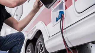 A man with his landstream camper, to which he connects a charging cable for power supply.