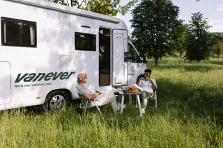 zwei Männer sitzen vor dem Camper Corsica im Grünen