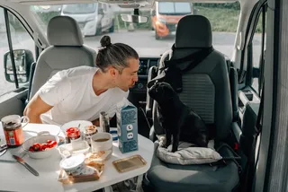 Mann mit Hund im Camper beim Frühstück auf Campingplatz