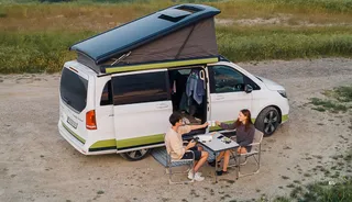 Pärchen sits in front of the camper on camping chairs in nature
