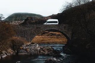 A VW Grand California crosses a river using a bridge.