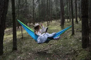 Eine Frau liest in einer Hängematte im Wald.