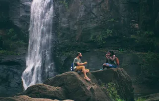 Two friends are sitting in front of a waterfall.