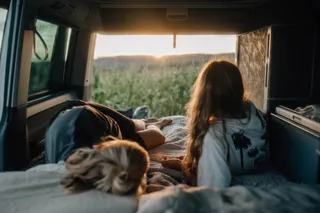 At the camping in Albania are two girls in the parked camper, the tailgate is open and you can see a field.