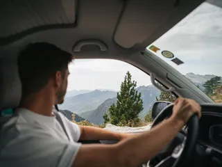 A man drives a van at the campsite in Albania and looks through the window on a forested mountain scenery.