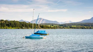 Two blue boats swim on the Riegsee in front of the mountain scenery and the tree-lined shore on the water