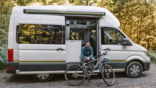 A man stands with his campervan at Camping Brugger am Riegsee campsite: before him his bike with which he starts a tour