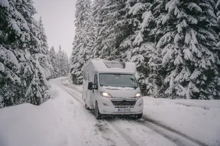 A Mooveo camper runs through a snowy forest.