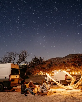 Campers sit at the campfire under a starry sky.