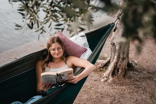 A woman is reading in a hammock.
