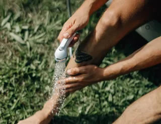 One person washes the legs in the meadow with the shower head of the camper: It is also necessary to keep the drinking water in the camper germ-free and free from the biofilm.