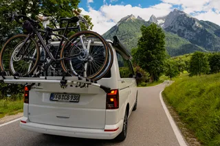 Bicycle camper photographed on a road in the mountains with loaded bicycle carrier from behind, while driving past wet meadows