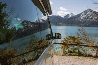 An off camper in front of the shore of a lake, where the water is reflected