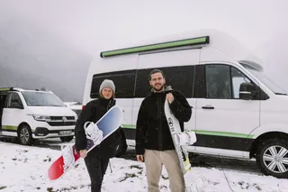 Two people with snowboard in front of Off Camper in the snow