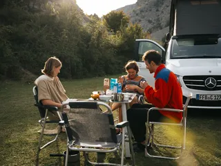 Keeping the drinking water fresh and clean is also important for cooking: A group of friends sits around their camping table on a sunny meadow next to their camper. and breakfast