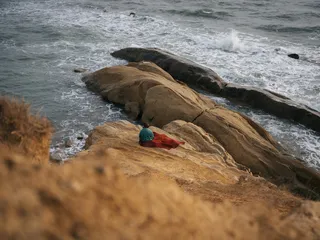 A woman sits on a picnic blanket on rocks that protrude into the sea