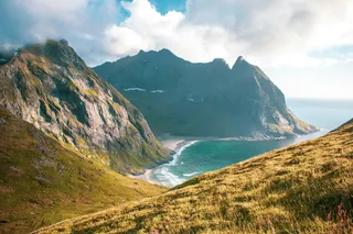 The lofotens in Norway from above, you can see high mountains and a beach and blue sea. Beautiful places in Norway can be found in this article.