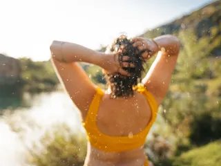 A woman in bathing clothes shakes the water out of the hair after swimming.