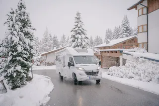 A Mooveo camper drives a road along the snowy surroundings during winter camping.