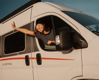 Eine Frau streckt den Kopf und den Arm aus dem Camperfenster