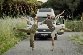 A Grand California Van is parked on a rural road. Two people posing and laughing.