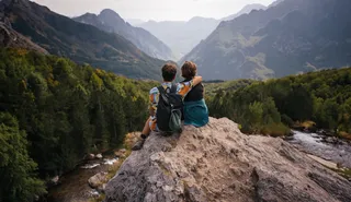 Two friends sit on a rock while hiking at their Albania round trip arm and look at the views of the mountains.