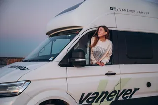 A woman is looking out of the camper window at sunset