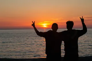 A gay couple on their trip with the camper: before sunset by the sea they show a peace sign.