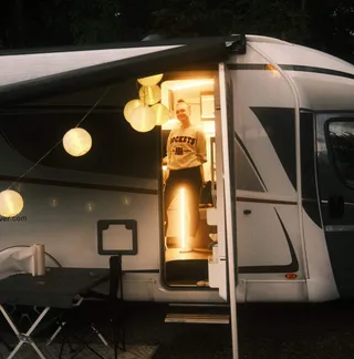 A woman is standing in the open, illuminated door of a white Vanever Corsica model motorhome.
