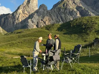 Friends are preparing breakfast on a hill with the Dolomites in the background