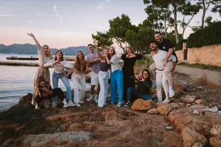 A group of friends celebrates on the beach and shows hearts with their hands in the camera.