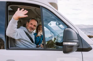 An older couple wins from their off camper's window.